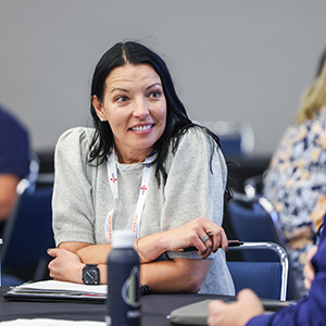 professional woman sitting at table holding pen over notebook while networking with the person sitting next to her